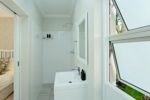 Baño blanco con lavabo y espejo en Tehillah Guest House, en George