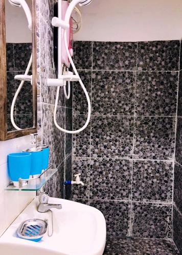 a bathroom with a white sink and a black tiled wall at Lanzones Cabana in Mambajao
