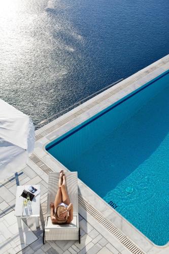 a woman sitting in a chair next to a swimming pool at Homeric Poems in Fira