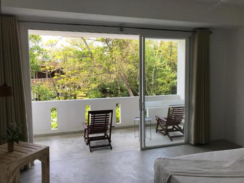 1 dormitorio con balcón con 2 sillas y puertas correderas de cristal en Jippie The Villa, en Hikkaduwa