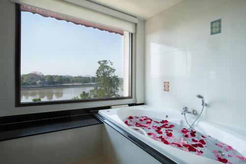 ein Badezimmer mit einem großen Fenster und einer Badewanne mit roten Blumen darauf in der Unterkunft The Imperial River House Resort, Chiang Rai in Chiang Rai