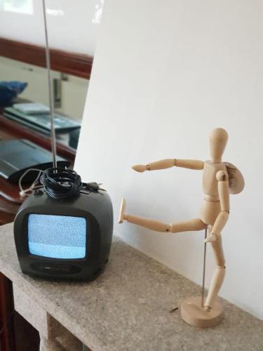 a wooden mannequin standing next to a small television at Yard in Amora