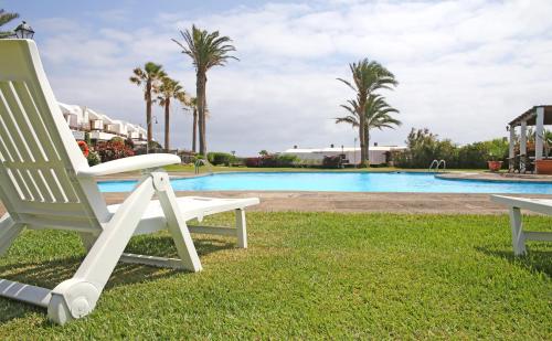 a white chair sitting in the grass near a swimming pool at Vivienda Vacacional Balcón sobre el Mar in Los Cancajos