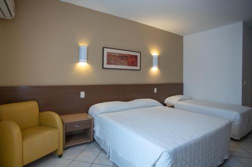 um quarto de hotel com duas camas e uma cadeira em Atobá Praia Hotel em Balneário Camboriú