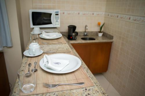 um balcão de cozinha com pratos e utensílios e um micro-ondas em Gloria Garden Suites em Macaé