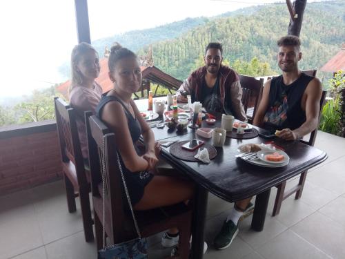 Puri Sunset Homestay في موندوك: مجموعة من الناس يجلسون على طاولة يأكلون الطعام
