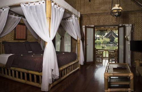 a bedroom with a canopy bed with white curtains at Kampung Sampireun Resort & Spa in Garut