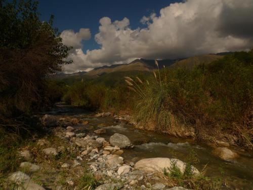 un río con rocas, árboles y montañas en el fondo en Samsara Traslasierra en Los Hornillos