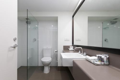 a bathroom with a toilet, sink, and mirror at Mercure Sydney Parramatta in Sydney