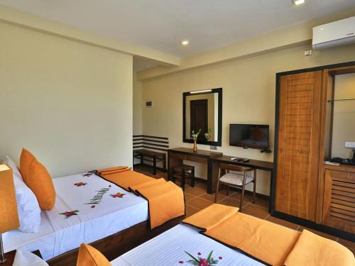 a room with two beds and a desk and a television at ROYAL KASHYAPA - Habarana in Habarana