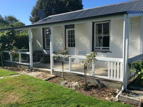 a white house with a porch with trees in the yard at Granny Stringer’s Cottage in Roxburgh