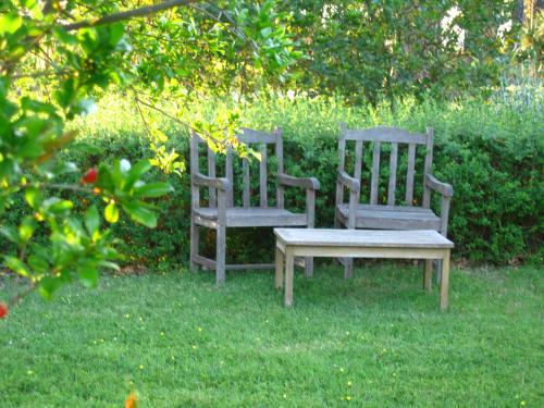 two wooden chairs and a bench in the grass at Villa Acquaviva Wine Resort in Montemerano