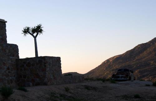 a car parked next to a stone wall with a palm tree at Jakkalswater guest farm in Nababeep