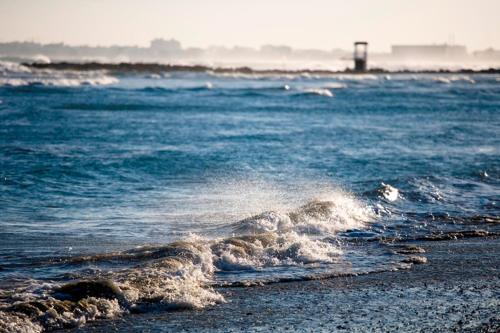 a wave in the ocean with a lighthouse in the background at Blue Serenity Complex in Larnaka
