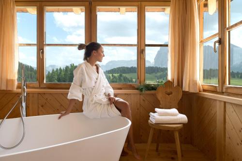 a woman sitting on a bath tub in a room with windows at Sporthotel Sonne in Alpe di Siusi