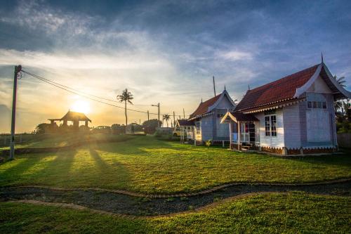 a house on a field with the sun setting behind it at Umbut Bayu in Dungun