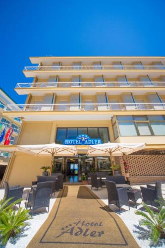 a hotel with chairs and umbrellas in front of it at Hotel Adler in Gabicce Mare