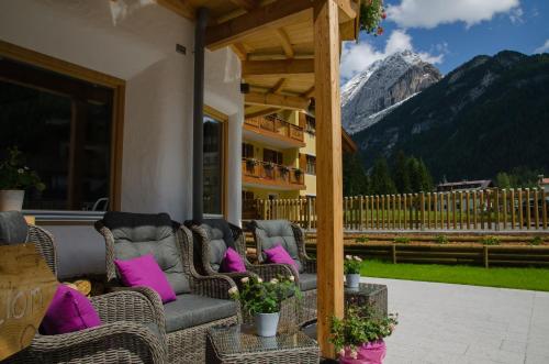 a porch with wicker chairs with pink pillows and a mountain at Chalet Vites Mountain Hotel in Canazei