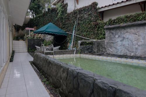 einen Pool mit Sonnenschirm neben einem Haus in der Unterkunft Urbanview Hotel Mon Bel Cibodas in Gegarbensang