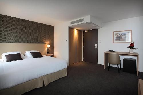 サン・ペ・シュル・ニヴェルにあるLogis Hotel de la Nivelleの大きなベッドとデスクが備わるホテルルームです。