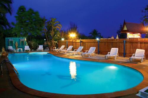 a large swimming pool with chairs and a fence at Pongphen Guesthouse - SHA Plus Certified in Kanchanaburi