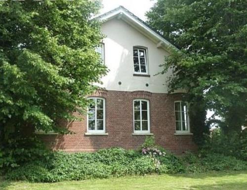 ein rotes Backsteinhaus mit zwei Fenstern und Bäumen in der Unterkunft Landhaus Ferienwohnung Wagner in Weener