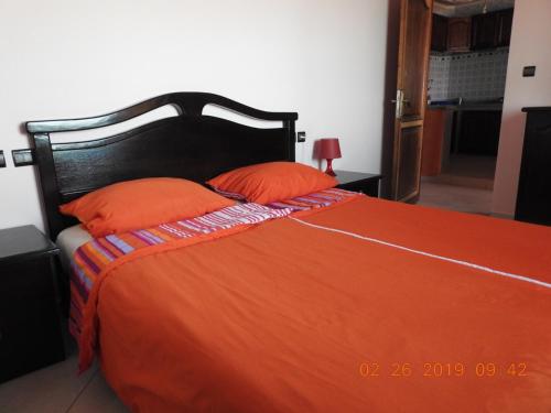 a bed with an orange blanket and two orange pillows at Atlantica-Home in Aourir