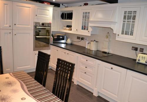 a kitchen with white cabinets and a table and chairs at Justa Cottage in Shaldon