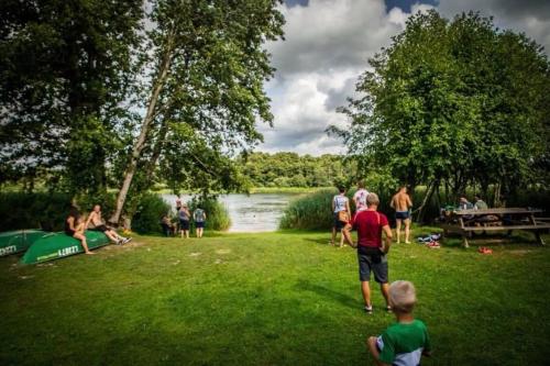 a group of people standing in the grass near a lake at Kempings Raganas slota in Vārve