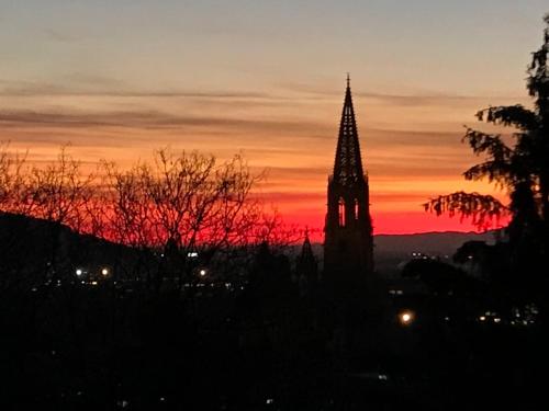 uma torre de relógio com um pôr-do-sol ao fundo em Ferienwohnung-Freiburg-Exklusiv em Friburgo em Brisgóvia