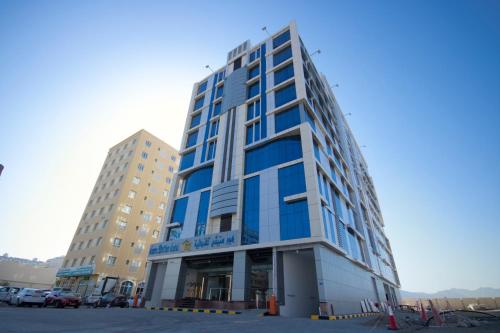 a tall building with blue windows in a parking lot at Home Station Hotel in Muscat
