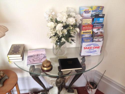 einen Glastisch mit einer Vase aus Blumen und Büchern in der Unterkunft Malvern Lodge Guest House- Close to Beach, Train Station & Southend Airport in Southend-on-Sea