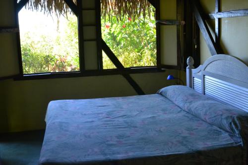 a bed in a room with two windows at Treetops B & B Inn in San Juanillo