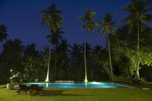 a pool with chairs and palm trees at night at Garden Villa Ronnaduwa in Hikkaduwa