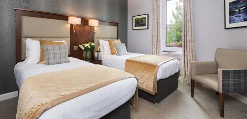 una habitación de hotel con 2 camas y una silla en Rosehill Guest House, en Pitlochry