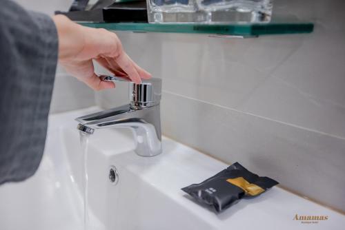 a person is reaching for a faucet on a sink at Amamas Boutique Hotel Kuching in Kuching