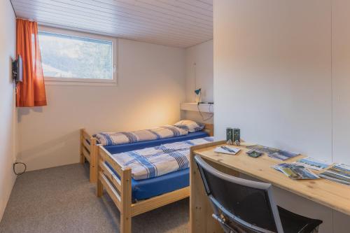 a room with two beds and a desk with a computer at Mountain Lodge Backpackercamp in Lenk