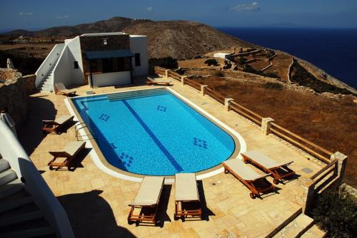 a large swimming pool with chairs and the ocean at Anemousa Hotel in Chora Folegandros