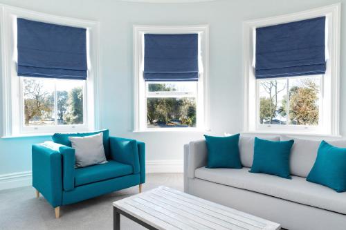 a living room with blue chairs and a couch and windows at Sandhills Apartments, Mudeford in Christchurch