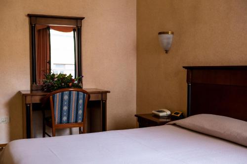 una camera con un letto e una sedia e una finestra di Hotel Astor a Piacenza