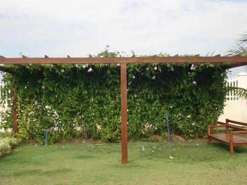a pergola with a bench in front of a green hedge at Villaggio dos Ventos in Arraial do Cabo