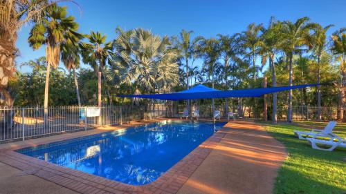 a swimming pool with a blue umbrella and palm trees at Discovery Parks - Katherine in Katherine