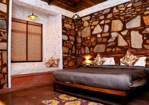a bedroom with a stone wall with a bed and a window at Riverarch Greenfields Resort in Chandwaji