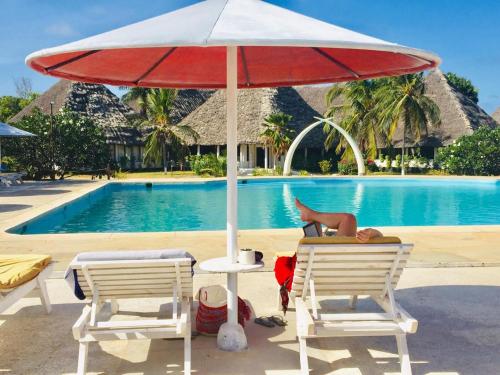 a red umbrella and two chairs next to a pool at Karibuni Hotel & Villas in Mambrui