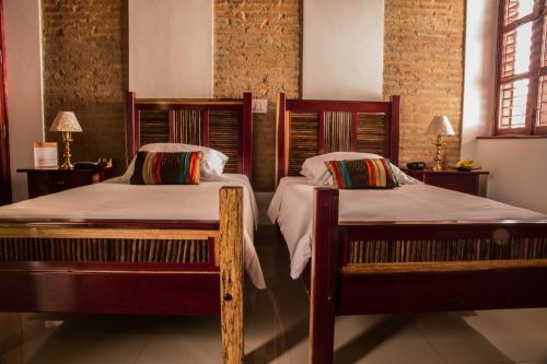 two beds in a bedroom with brick walls and windows at Casa de Isabella, a Kali Hotel in Santa Marta