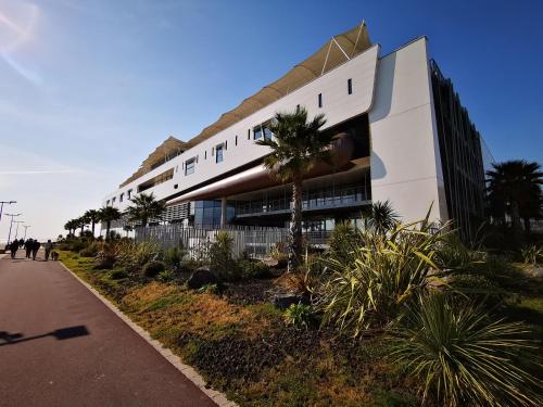un grand bâtiment blanc avec des palmiers devant dans l'établissement Studio 34 curistes/vacanciers, à Balaruc-les-Bains