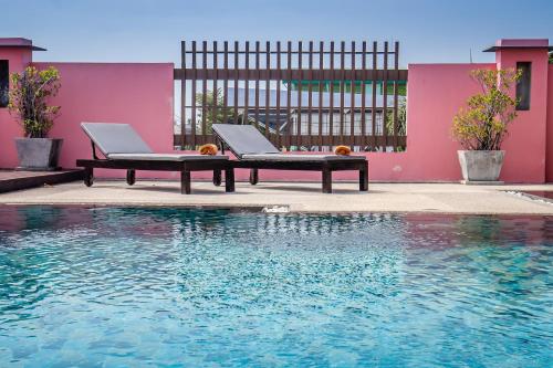a pool with two lounge chairs next to a pink building at Ratana Hotel Chalong in Rawai Beach