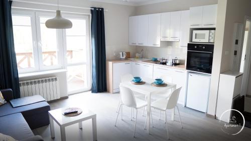 a kitchen with white cabinets and a white table and chairs at Apartament Siódemka in Pisz