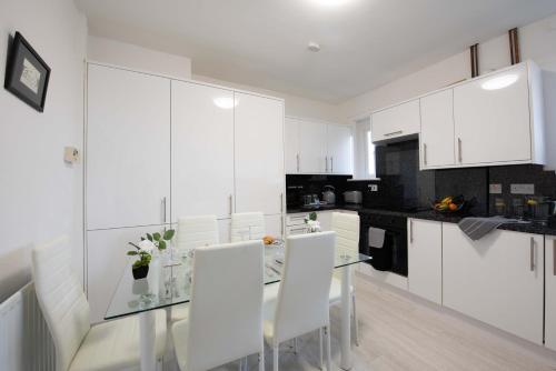 a white kitchen with a glass table and white chairs at PREMIER - Garfield Apartment in Bellshill