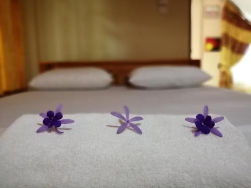 three purple flowers sitting on a white bed at Viveka Inn Guest and Yala Safari in Tissamaharama